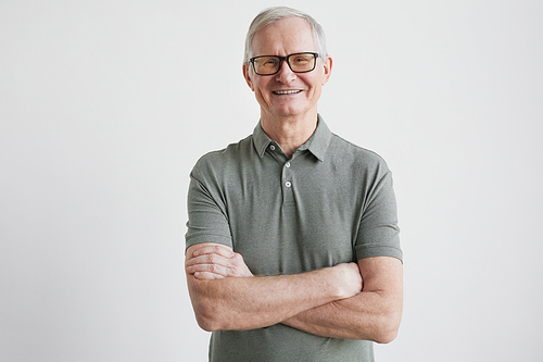 Minimal waist up portrait of smiling senior man looking at camera while standing with arms crossed against white background