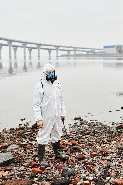 Full length portrait of male worker wearing hazmat suit by water outdoors, industrial waste concept, copy space
