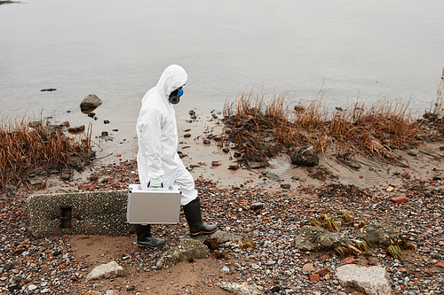 High angle portrait of male worker wearing hazmat suit walking by water outdoors, industrial waste concept, copy space