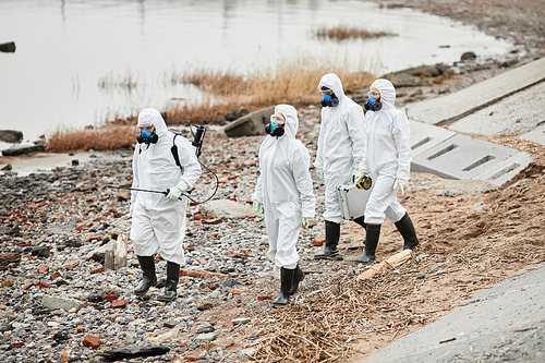 Group of workers wearing hazmat suits walking by water outdoors, toxic waste concept, copy space