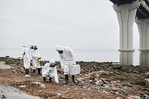 Wide angle view at group of workers wearing hazmat suits gathering samples of soil by water outdoors, toxic waste concept, copy space