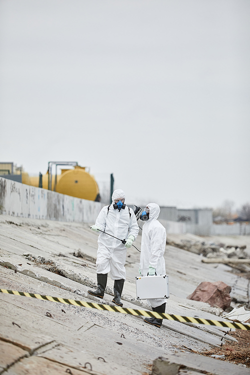 Full length portrait of two people wearing hazmat suits collecting probe samples in industrial area, toxic waste concept