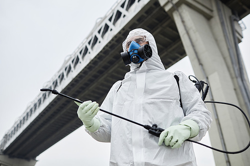 Industrial low angle portrait of man wearing hazmat suits standing under bridge, copy space