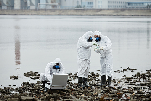 Group of people wearing hazmat suits collecting probes by water, toxic waste and pollution concept, copy space