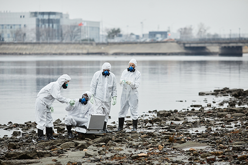 Wide angle view at group of people wearing hazmat suits collecting probes by water, toxic waste and pollution concept, copy space
