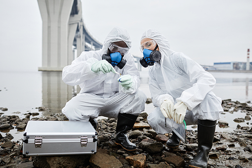Two people wearing hazmat suits collecting probes by water, toxic waste and pollution concept, copy space
