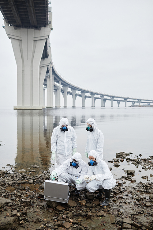 Vertical full length view view at group of people wearing hazmat suits collecting probes by water, toxic waste and pollution concept