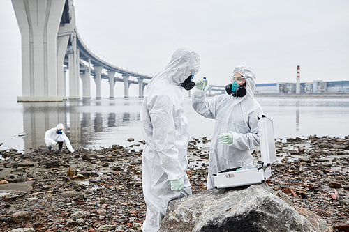 Waist up portrait of workers wearing hazmat suits collecting probes by water, toxic waste and pollution concept, copy space