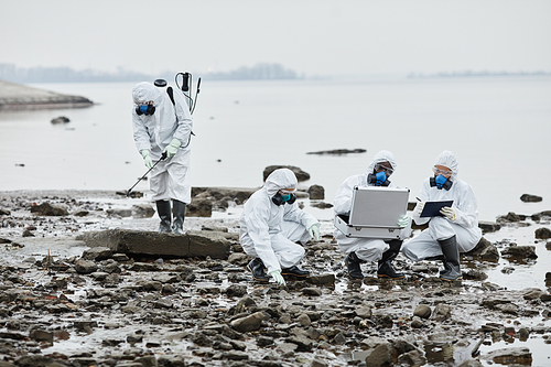 Group of workers wearing hazmat suits collecting samples by water, toxic waste and pollution concept, copy space