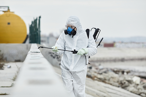 Portrait of worker wearing protective suit disinfecting industrial area while walking towards camera, copy space