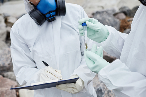 Close up of two scientists wearing hazmat suits collecting samples outdoors, toxic waste and pollution concept