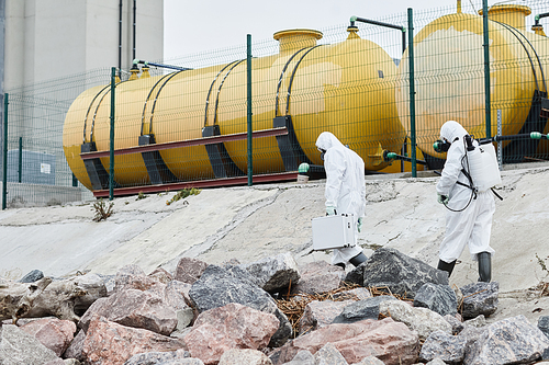 Wide angle view at two scientists wearing hazmat suits collecting samples outdoors, toxic waste and pollution concept, copy space