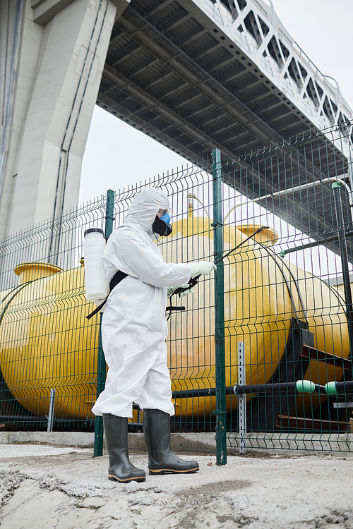 Full length portrait of worker wearing protective suit disinfecting industrial area