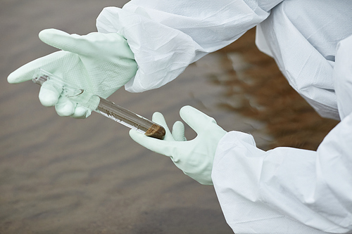 Close up of unrecognizable scientist wearing hazmat suit collecting water probes, focus on gloved hands holding test tube