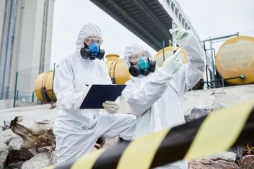 Two people in hazmat suits working at ecological disaster site, toxic waste and pollution concept, copy space