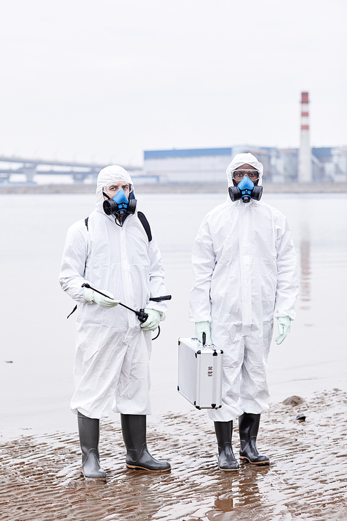 Vertical full length portrait of two people wearing protective suits and looking at camera outdoors at industrial site