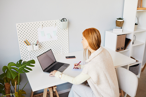 High angle portrait of young red haired woman using laptop or studying at minimal home workplace, copy space