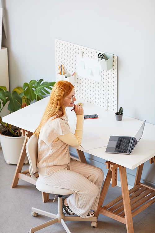 High angle portrait of adult red haired woman using laptop while working at home office, copy space