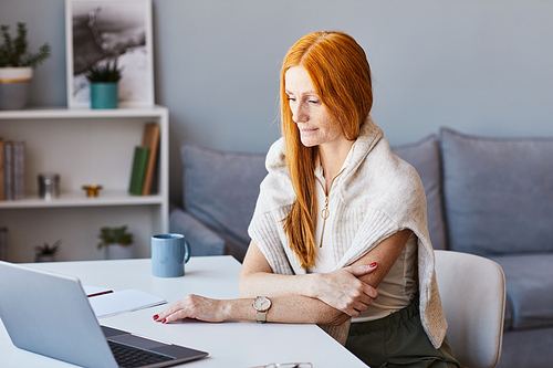 Portrait of elegant red haired woman using laptop while working at home office, copy space