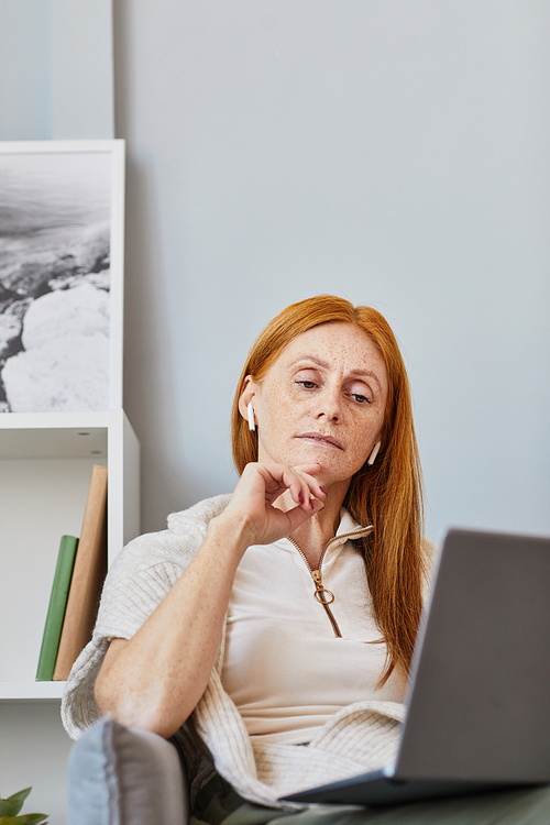 Vertical portrait of adult red haired woman using laptop in online meeting at home