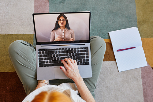 Top down view at unrecognizable young woman using laptop while studying online at home