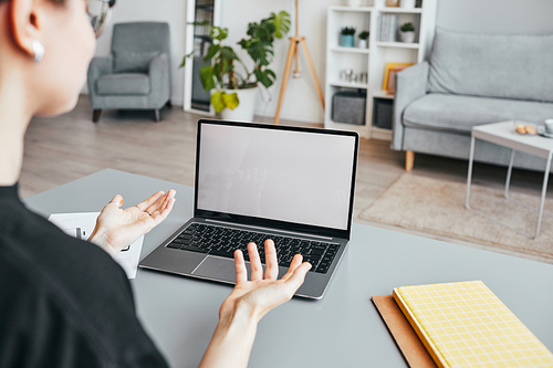 Close up of unrecognizable woman in online meeting gesturing while looking at blank laptop screen in home office, copy space