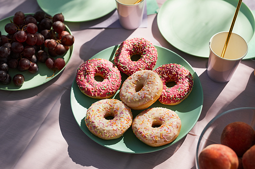 Close up of pink donuts on Summer picnic table outdoors decorated for Birthday party, copy space