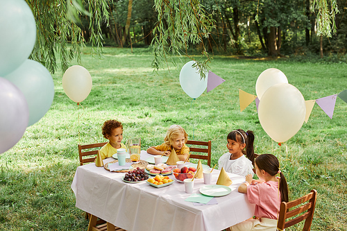 Group of kids at picnic table outdoors decorated with balloons for Birthday party in Summer, copy space
