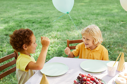 Two kids at picnic table outdoors decorated with balloons for Birthday party in Summer, copy space
