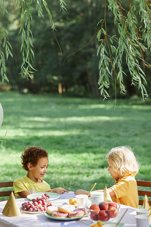 Vertical portrait of two little kids at picnic table outdoors enjoying Birthday party in Summer, copy space