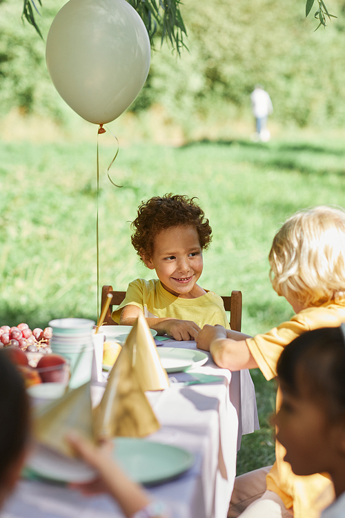 Diverse group of kids at picnic table outdoors decorated with balloons for Birthday party in Summer