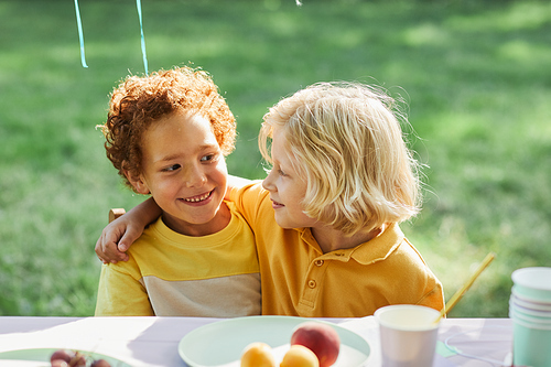 Portrait of two smiling boys embracing at picnic table outdoors while enjoying Birthday party in Summer, copy space