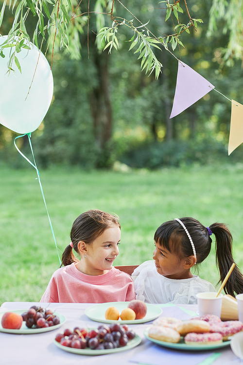 Vertical portrait of two little girls at picnic table outdoors enjoying Birthday party in Summer