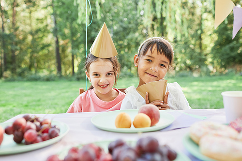 Portrait of two smiling little girls at picnic table outdoors enjoying Birthday party in Summer