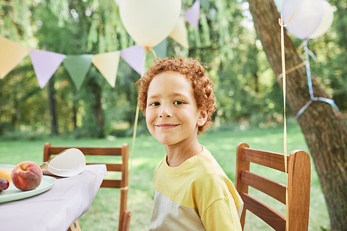 Portrait of smiling boy looking at camera at picnic table outdoors enjoying Birthday party in Summer