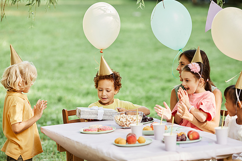 Side view portrait of group of kids enjoying outdoor Birthday party in summer and giving gifts