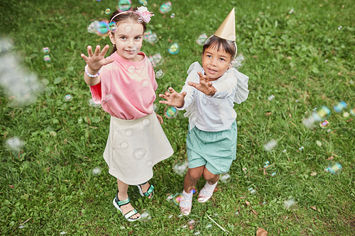 High angle portrait of two little girls playing with bubbles while enjoying Birthday party outdoors in Summer