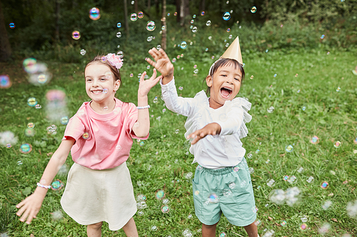 Portrait of two cute girls playing with bubbles while enjoying Birthday party outdoors in Summer