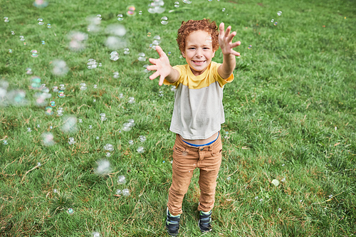 Full length portrait of smiling cute boy playing with bubbles while enjoying Birthday party outdoors in Summer
