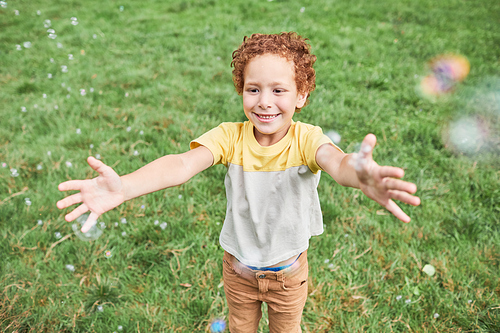 Portrait of cute boy playing with bubbles outdoors in park and smiling, copy space