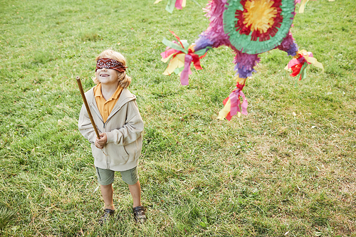 Portrait of boy playing pinata game at Birthday party outdoors and holding bat, copy space
