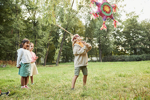 Full length portrait of boy playing pinata game at Birthday party outdoors and holding bat, copy space