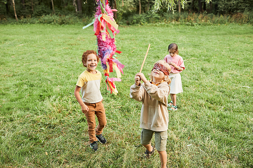 High angle portrait of boy playing pinata game at Birthday party outdoors and holding bat, copy space