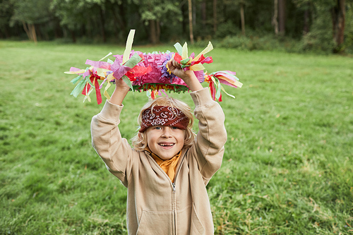 Waist up portrait of cue boy holding pinata and smiling at camera during Birthday party outdoors, copy space