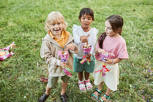 Full length portrait of three cute children holding sweets from pinata during Birthday party outdoors