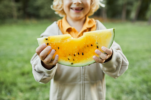 Close up of cute boy holding yellow watermelon outdoors and smiling at camera, copy space