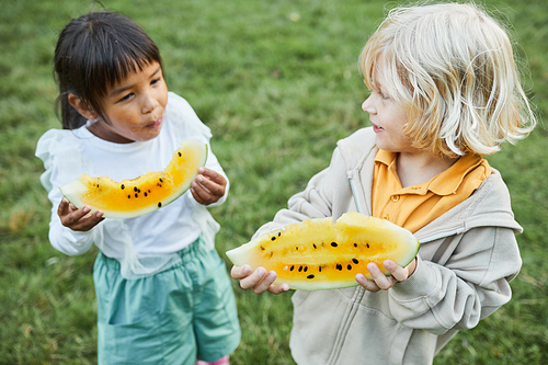 High angle portrait of two little kids eating watermelon outdoors nd smiling
