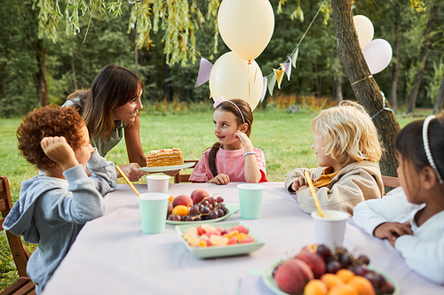 Portrait of young mother bringing Birthday cake to smiling girl during Birthday party outdoors, copy space