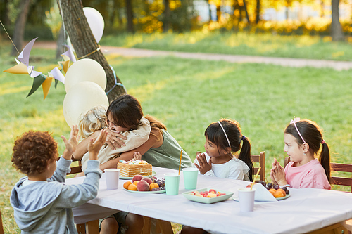 Portrait of mother embracing little son during Birthday party outdoors with friends, copy space
