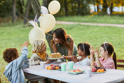 Portrait of smiling mother bringing Birthday cake to little boy during Birthday party outdoors, copy space